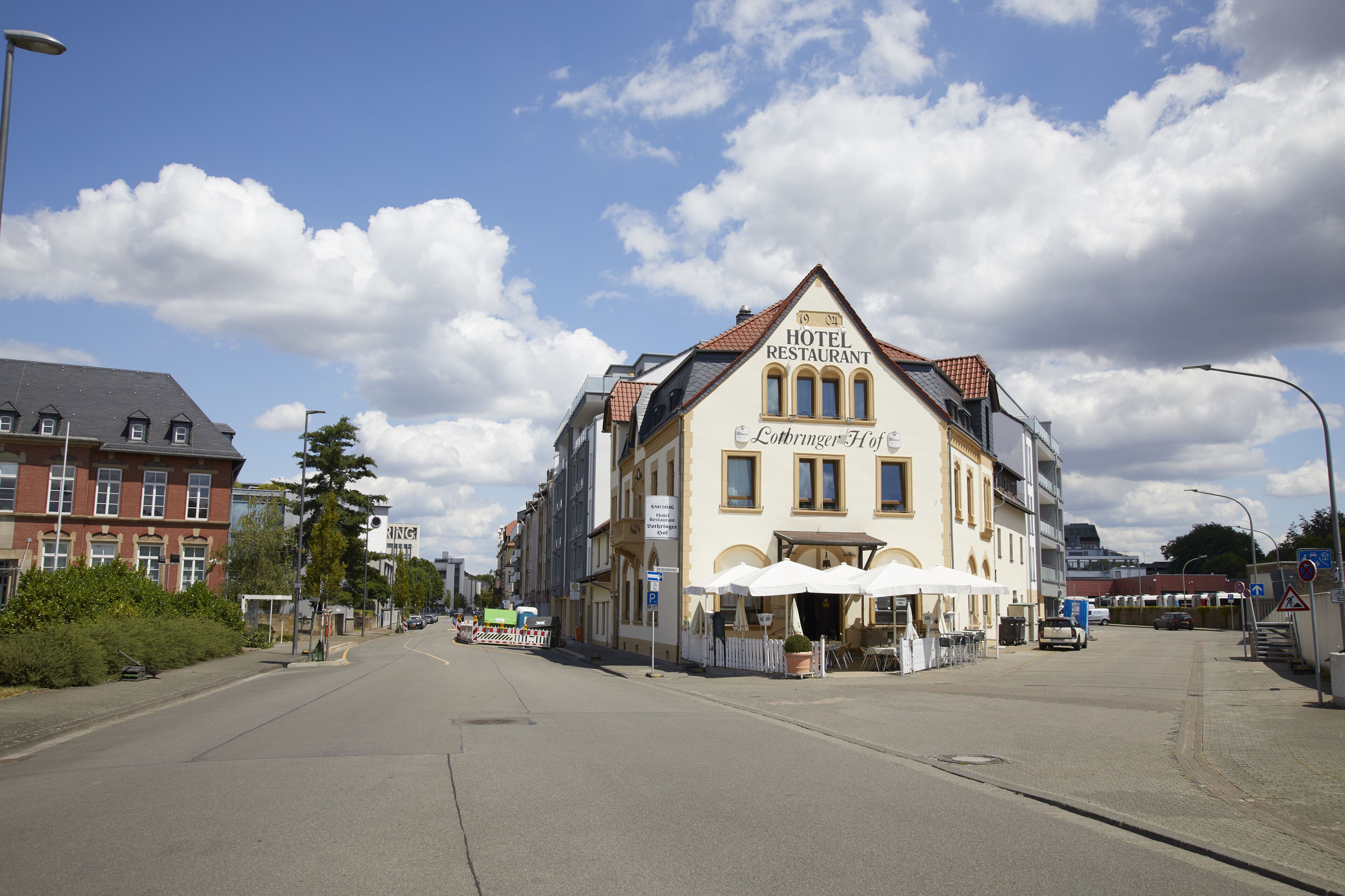 A hotel with a classic European architectural style, featuring a prominent signboard and a terrace with outdoor seating.