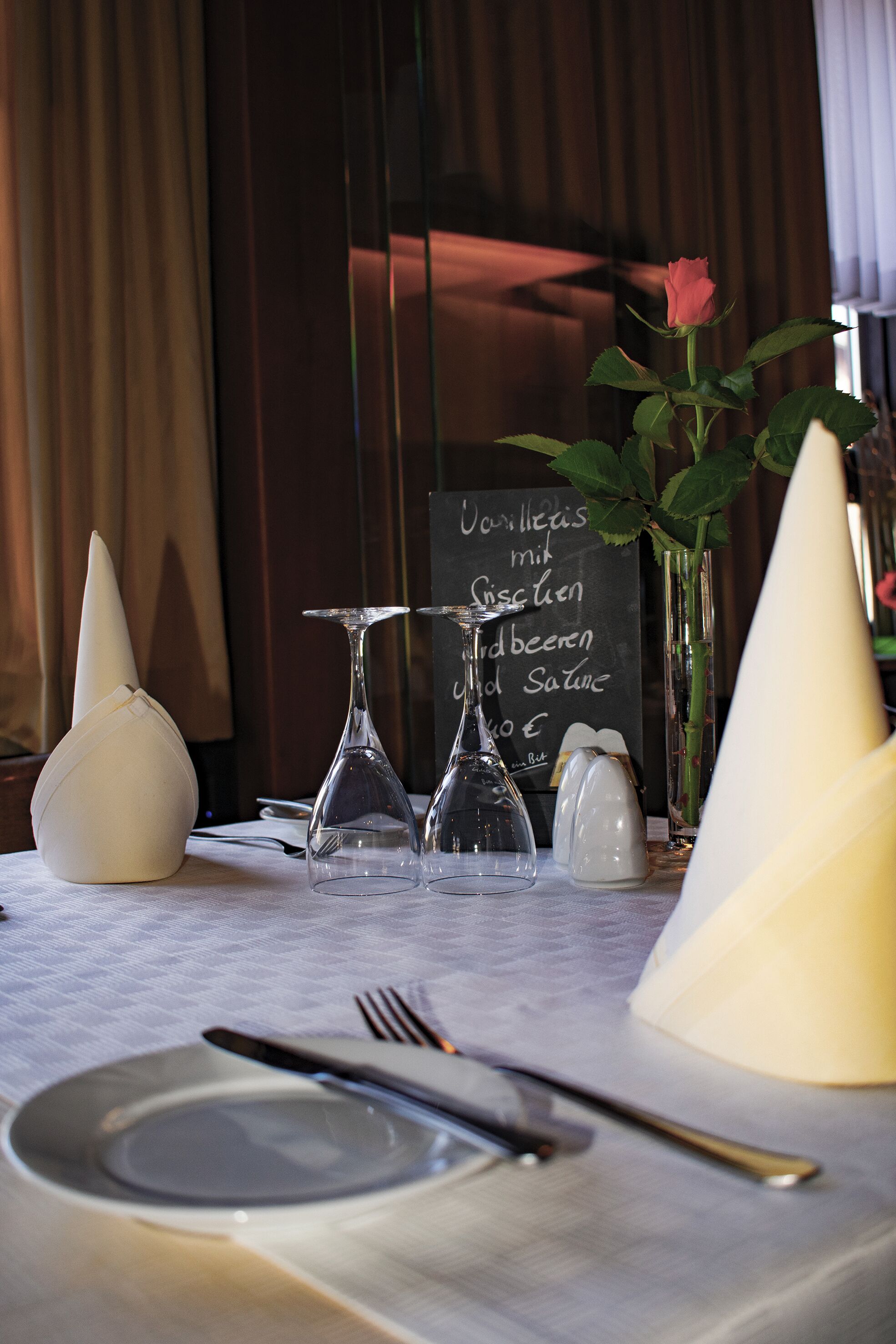 A dining table with a white tablecloth, a rose, a vase, and a menu board.