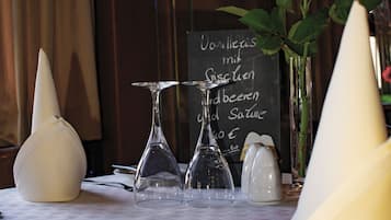 A dining table with a white tablecloth, a rose, a vase, and a menu board.