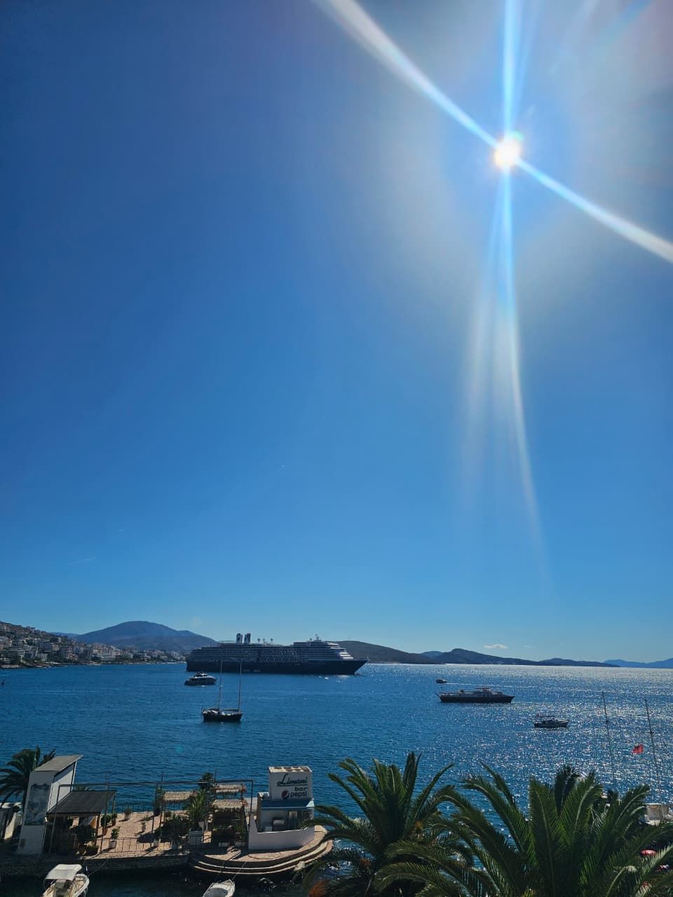 A clear view of a coastal marina with a large cruise ship docked, surrounded by smaller boats and a pepsi bar sign.