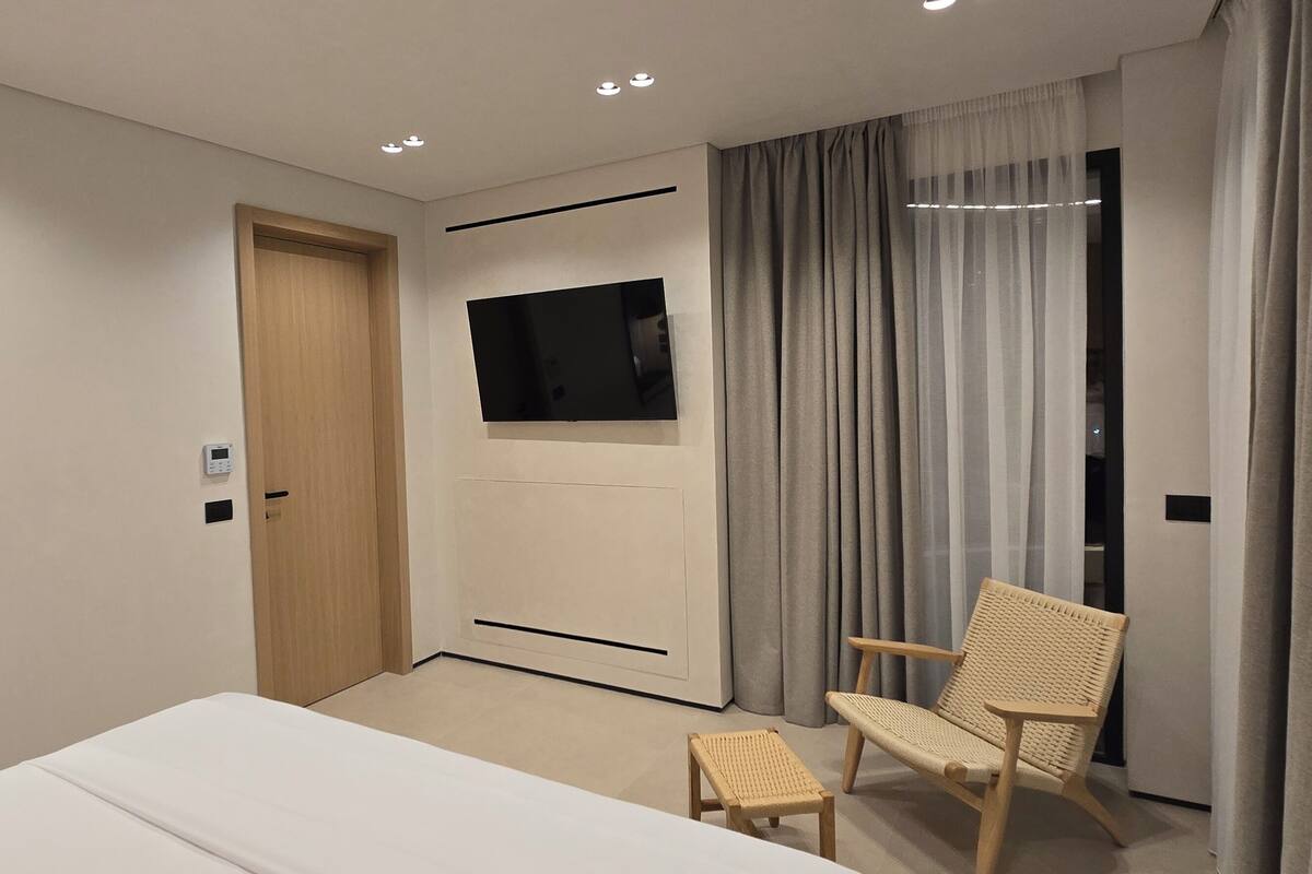 A modern hotel room with a bed, a chair, a TV, and a door.