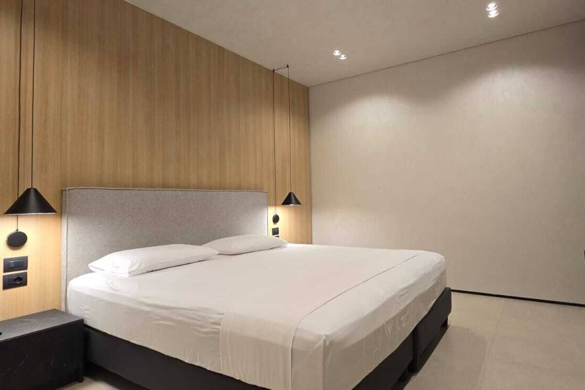 A modern bedroom with a large bed, two bedside lamps, and a wooden panel wall.
