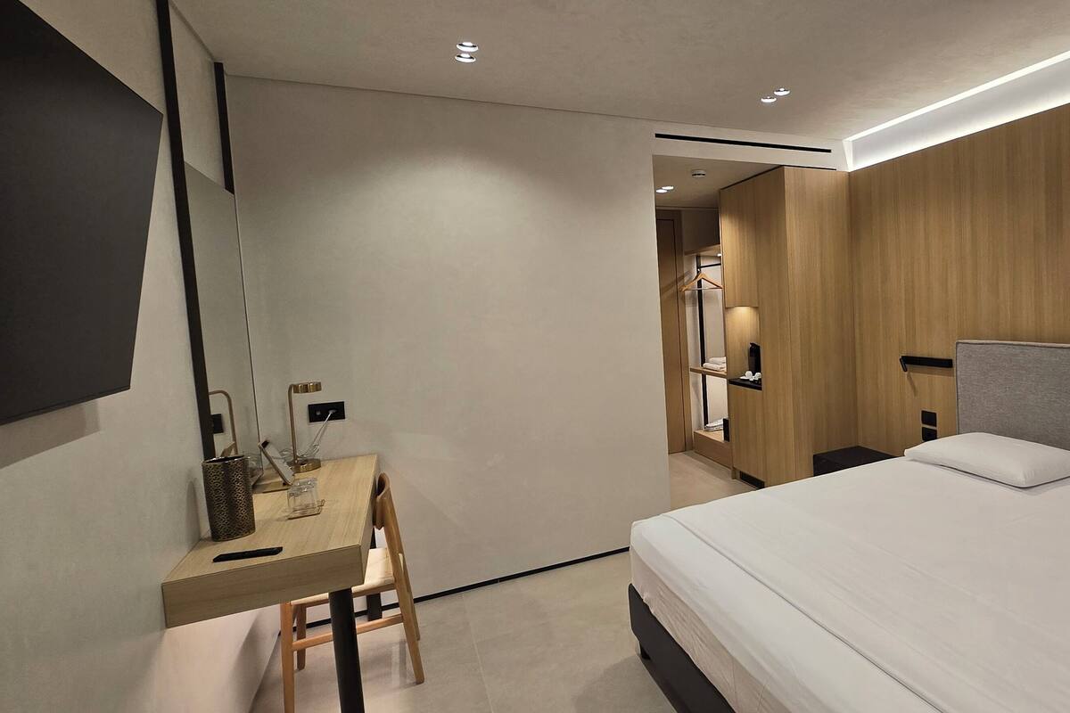 A modern hotel room with a large bed, a desk with a chair, and a mirror.