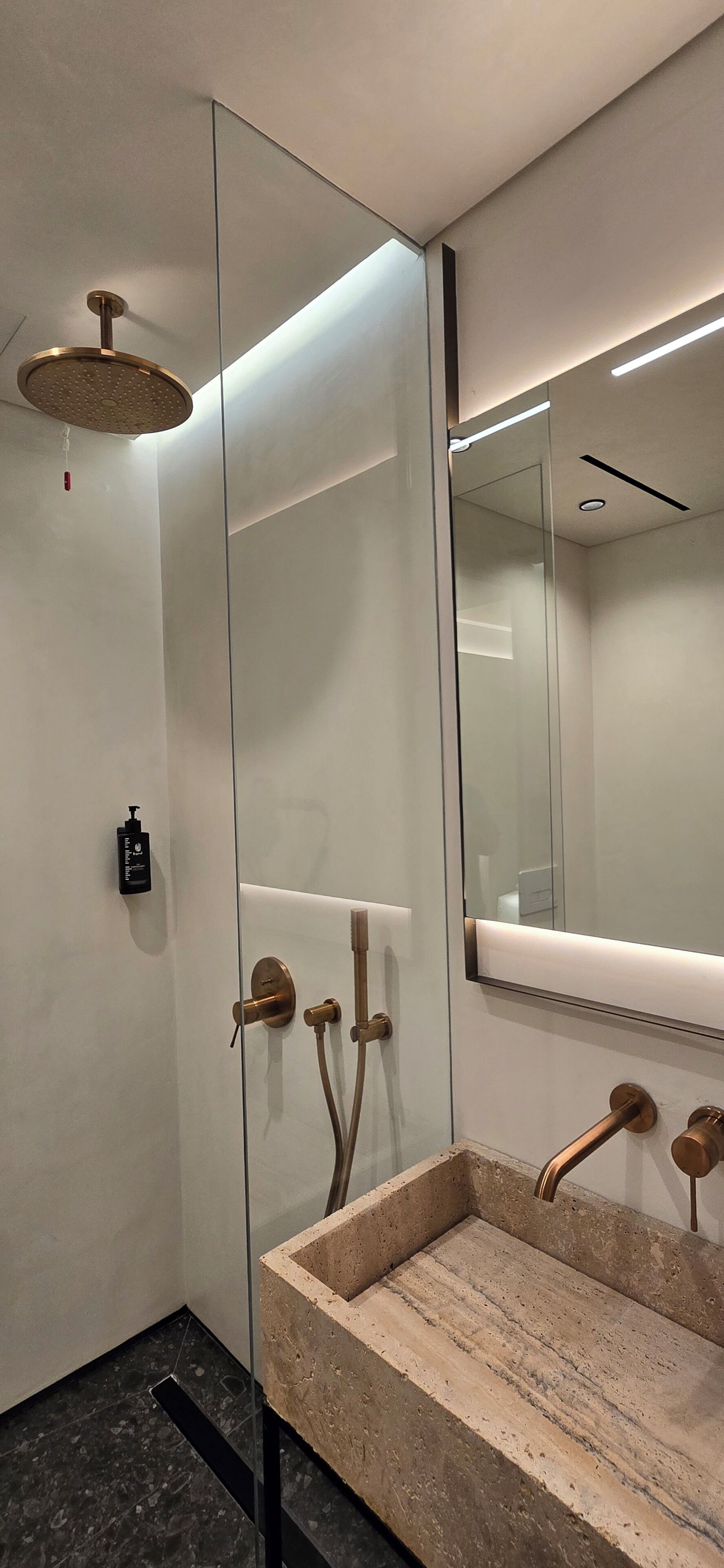 Ein modernes Badezimmer mit einer Duschkabine aus Glas, einem beige gefärbten Waschbecken mit Marmorplatte und einem großen Spiegel.