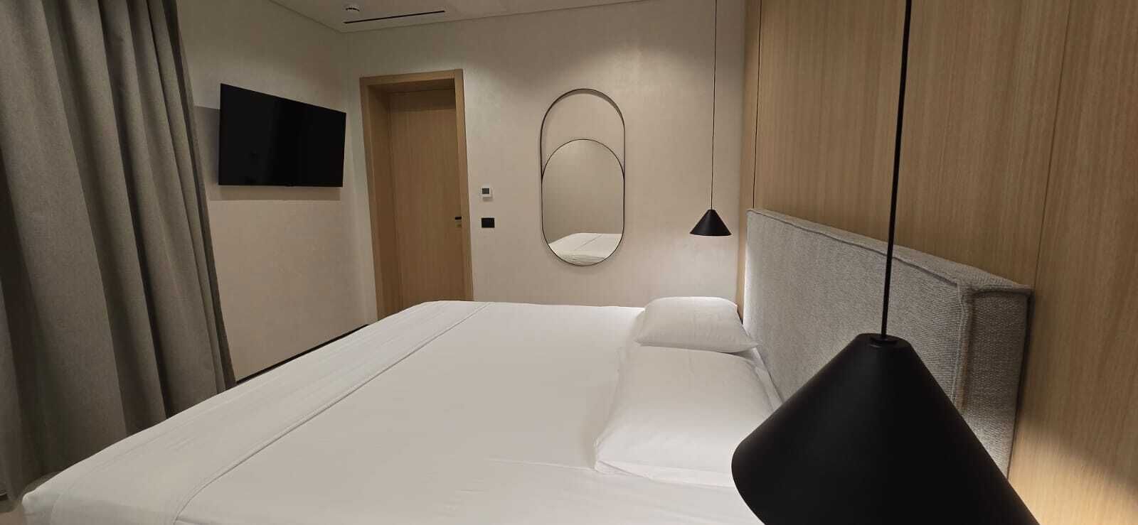 A hotel room with a large bed, a bedside table, a mirror, and a TV on the wall.