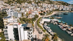 A coastal cityscape with modern buildings, a marina with boats, and a beach. - Lion Gate Hotel (Sarandë)