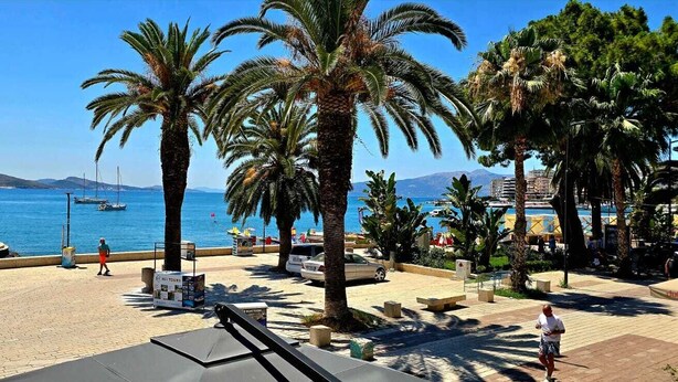 A coastal promenade with palm trees, a marina with boats, and a clear blue sky. - Lion Gate Hotel (Sarandë)