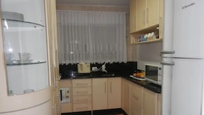 A compact kitchen with a refrigerator, microwave, and a small countertop. - Apto Praia Central Camburiu (Balneário Camboriú)