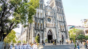 Una catedral histórica con un gran reloj, escalinatas que conducen a la entrada y una multitud de personas al frente.