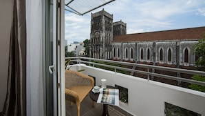 Un balcón con una silla de mimbre, una mesa con una taza y un plato, y vistas a un edificio histórico con ventanas arqueadas.