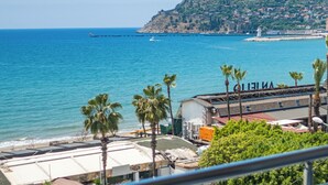 Un balcón con vista a una playa, una piscina y una colina distante.