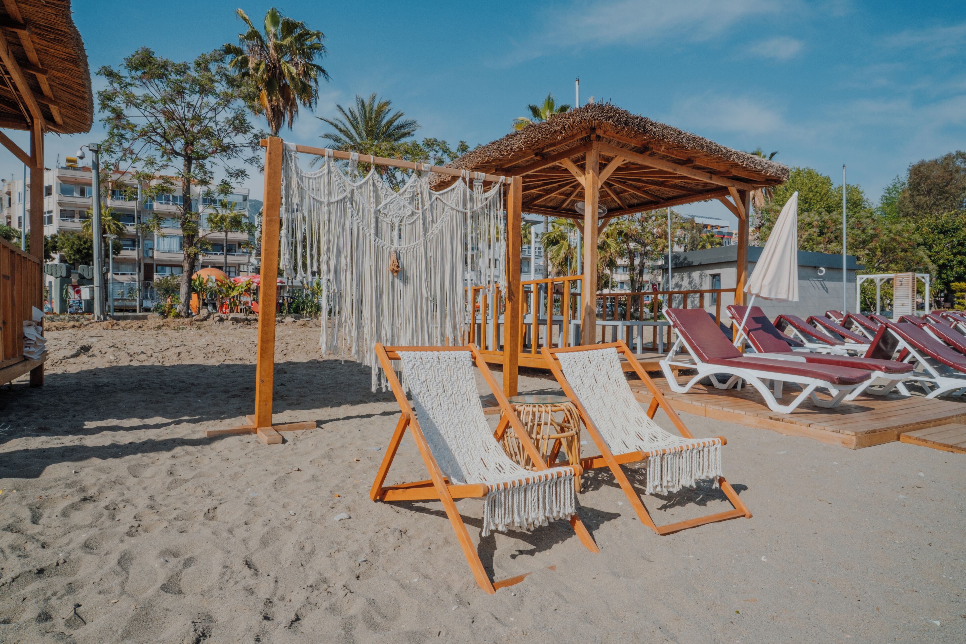 Un’area spiaggia con lettini di legno, un gazebo con tetto di paglia e un pannello decorativo in macramè.