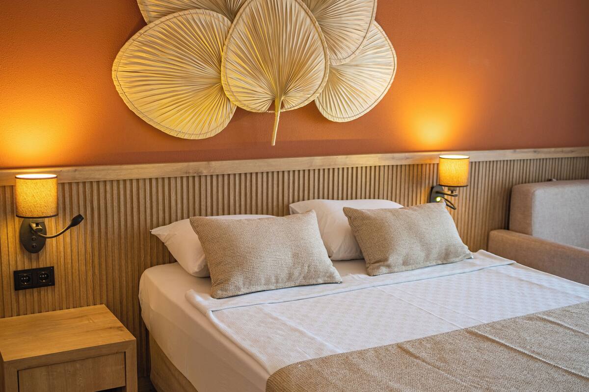 A hotel room with a bed, two bedside lamps, a nightstand, and a wall-mounted decorative light fixture.