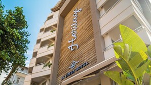 Un hotel con fachada moderna, un letrero llamativo que dice "By Cimen Hotel", y exuberante follaje en primer plano.