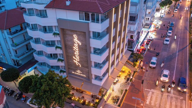 Un hotel con varios balcones, un llamativo letrero de neón y vista a la calle con coches aparcados y peatones.