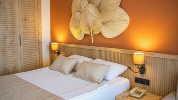 Una cama bien tendida con dos almohadas, un teléfono en la mesita de noche y lámparas fijadas a la pared.