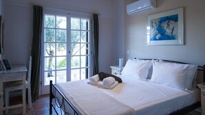 A bedroom with a bed, a desk, a chair, a window with curtains, an air conditioner, and a painting on the wall. - Penelope Dream Pool Villa (Kefalonia)