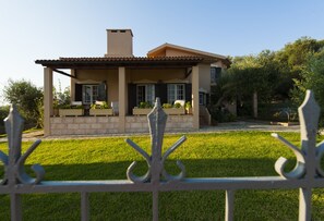 A two-story house with a tiled roof, a front porch with a bench, and a well-maintained lawn.