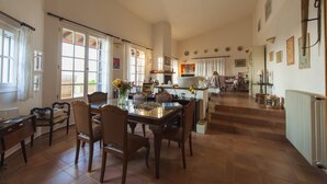 A spacious dining area with a wooden table and chairs, a kitchen in the background, and a staircase leading to another level. - Penelope Dream Pool Villa (Kefalonia)