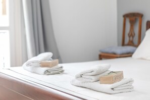 A neatly made bed with folded white towels and a wooden box labeled "Olive Soaps" on the bed.