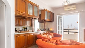 A kitchen with wooden cabinets, a countertop with various appliances, and a sofa in the adjacent living area.