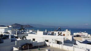 A coastal residential area with white buildings, solar panels, and a clear view of the sea and distant mountains.