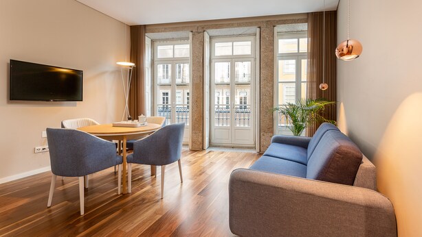 A modern living room with a wooden floor, a sofa, a dining table with chairs, and a TV mounted on the wall. - RS Porto Historic Center (Porto)
