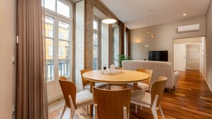 A modern dining area with a round table and six chairs, large windows, and a TV in the background. - RS Porto Historic Center (Porto)