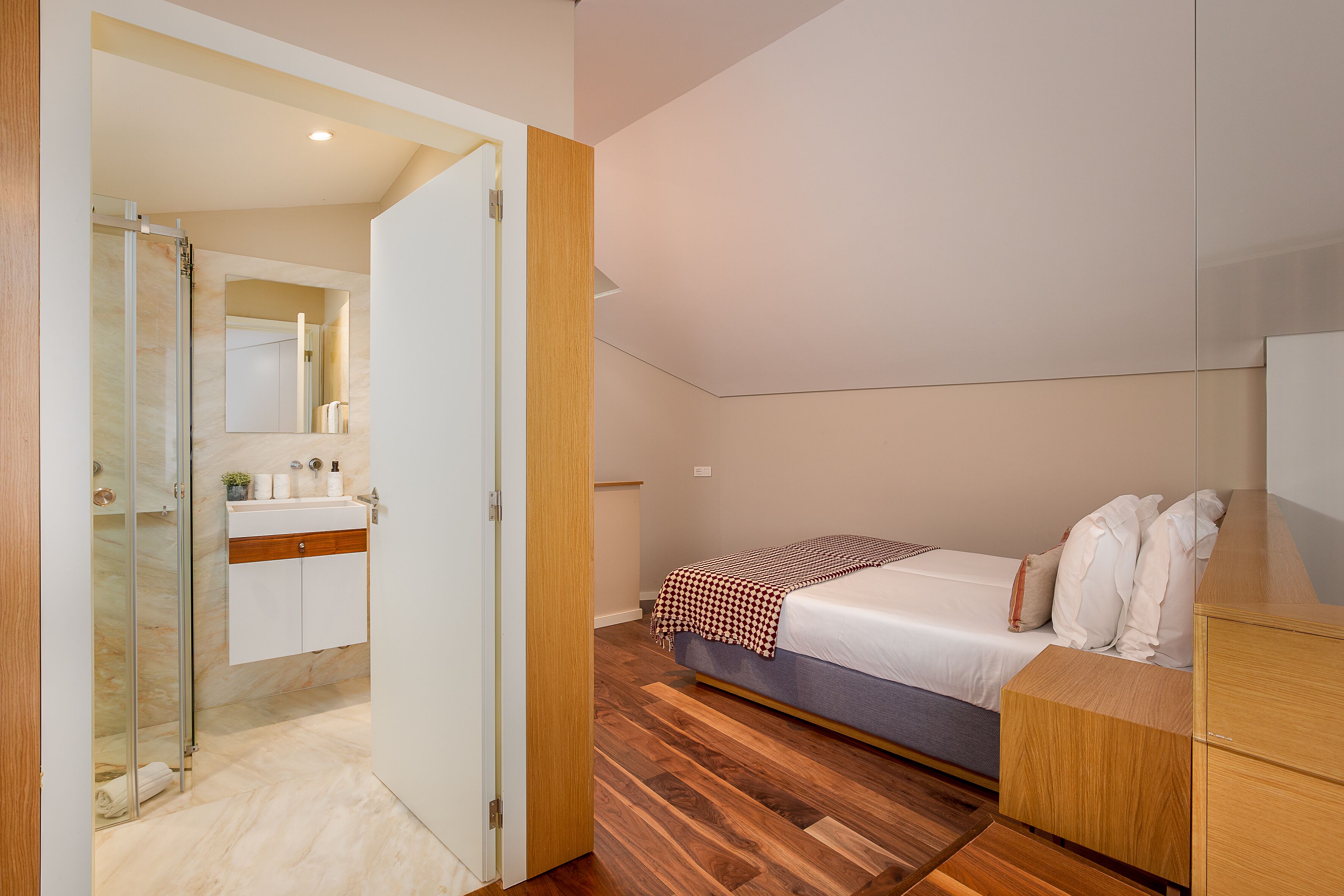 A bedroom with a bed, wooden wardrobe, and a bathroom with a mirror and sink.