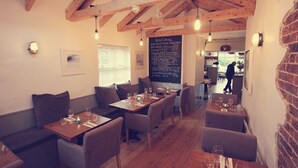 Un restaurant chaleureux avec des poutres en bois, des tables agrémentées de coussins et un menu écrit à la craie.