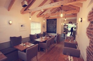 Un restaurant chaleureux avec des poutres en bois, des tables agrémentées de coussins et un menu écrit à la craie.