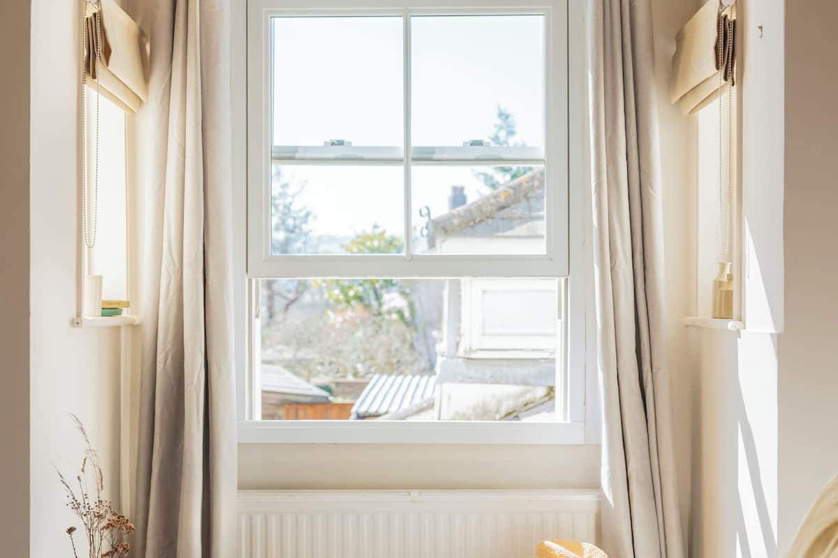 A room with a large window, a bed, a small table with breakfast items, and a radiator.