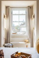 Une chambre dotée d’une grande fenêtre, d’un lit, d’une petite table avec des éléments pour le petit-déjeuner et d’un radiateur.