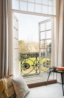 Une pièce avec une grande fenêtre, donnant sur un jardin, une petite table avec une tasse, et un banc avec des coussins.