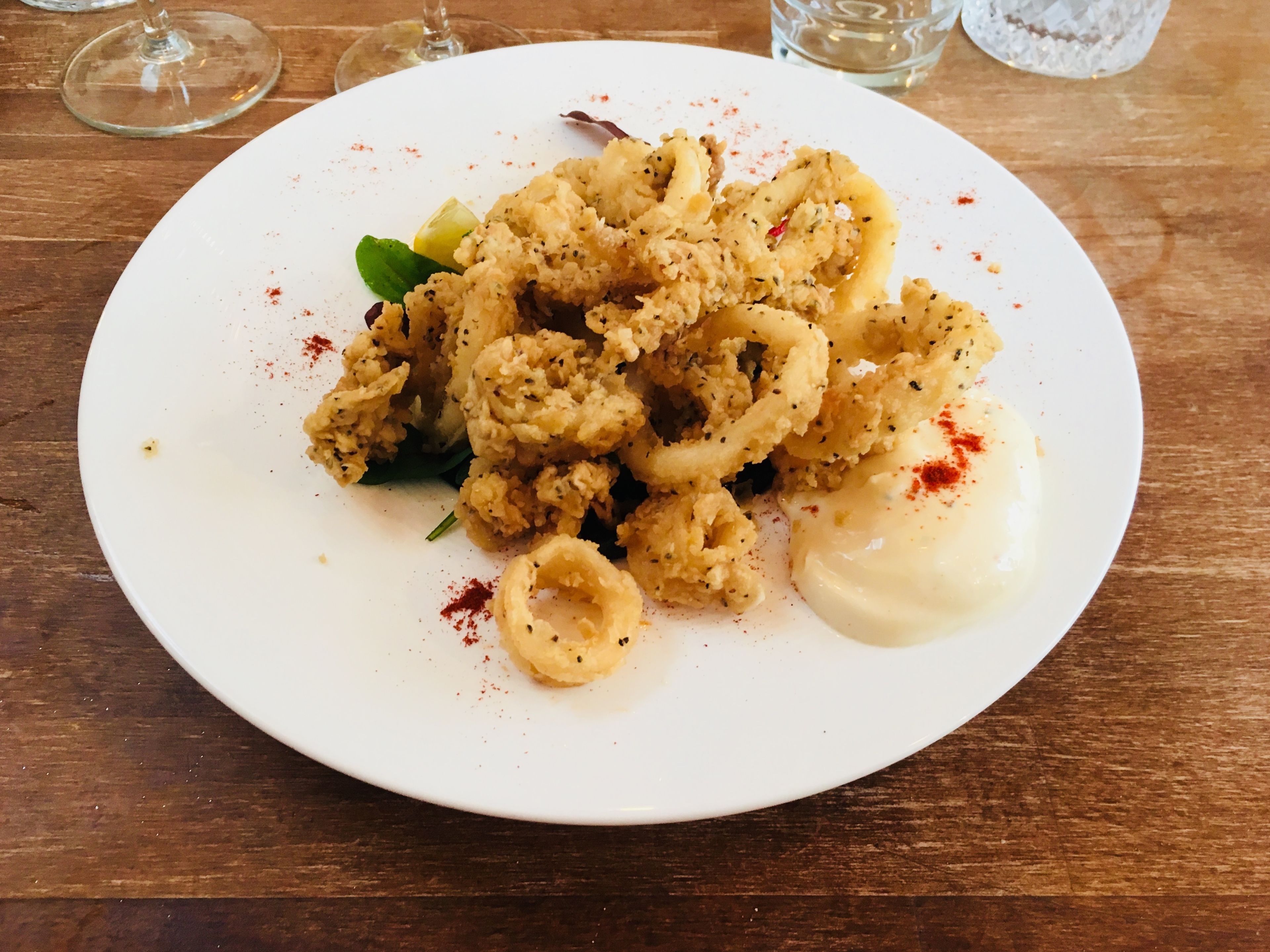 A plate of fried calamari with a creamy sauce and lemon on a wooden table.