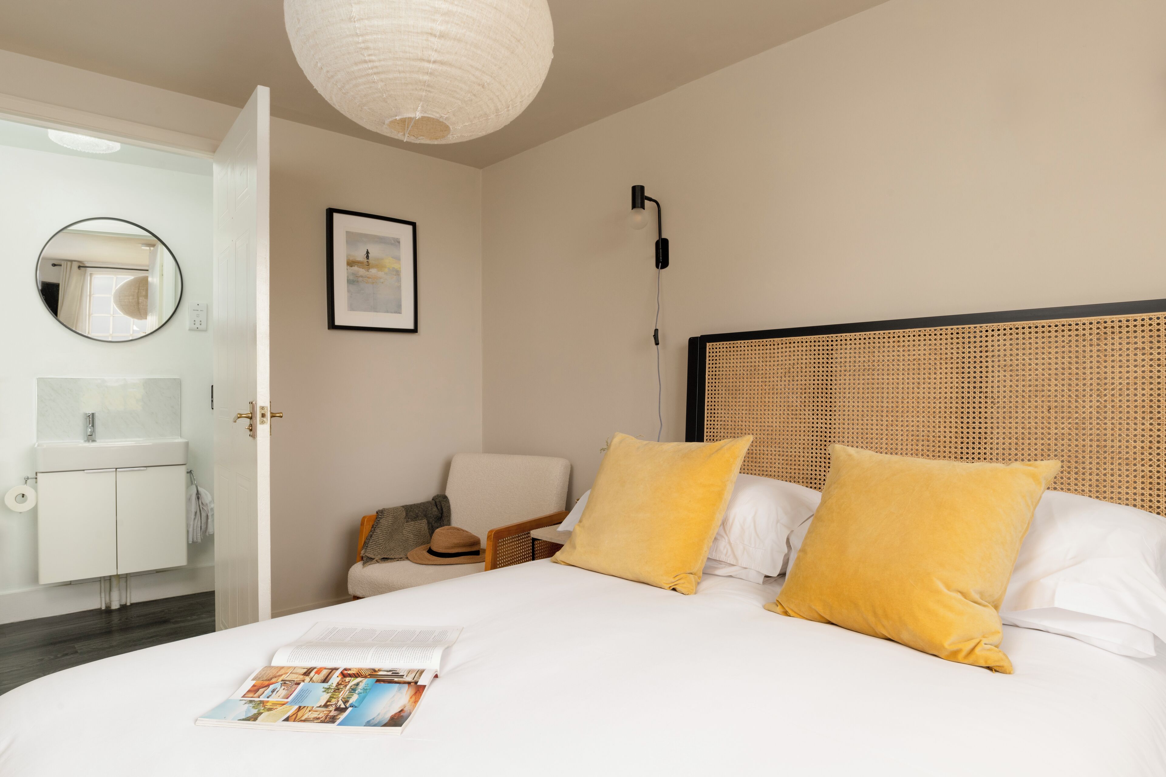 A neatly arranged bedroom with a bed, a chair, a bedside table, a mirror, and a wall-mounted light fixture.