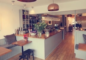 Eine moderne Bar mit Holztresen, Regalen voller Flaschen und einer Sitzgelegenheit mit einer Bank und einem Tisch.