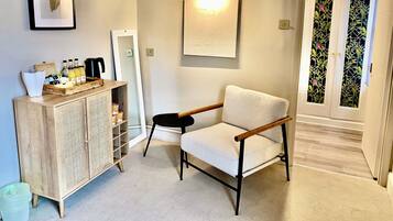 A room with a wooden cabinet, a white armchair, a small table, and a door with decorative glass panels.