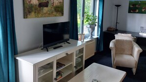 Un salón con un televisor sobre un mueble blanco, un sofá, una mesa baja y dos cuadros en las paredes.