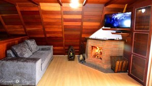 A cozy attic room with wooden walls, a fireplace, a sofa, and a TV. - Terrazzo dos Alpes (Camanducaia)