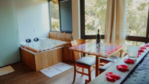 A room with a wooden bathtub, a glass table set with rose petals, and a bottle of wine. - Terrazzo dos Alpes (Camanducaia)