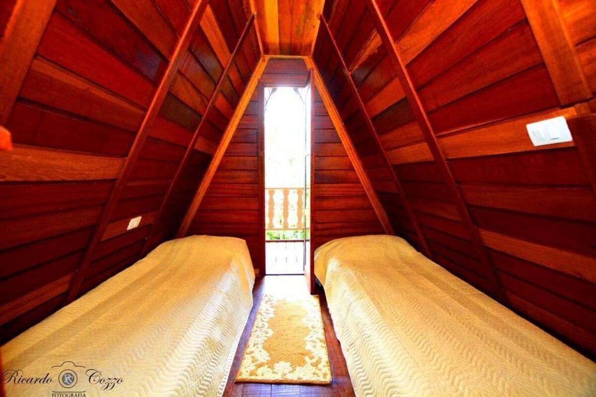 Ein Zimmer mit zwei Betten, einer schrägen Holzbalkendecke und Blick durch ein Fenster.