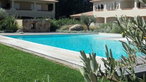 A swimming pool with a wooden deck, surrounded by greenery and two buildings with tiled roofs. - PORTO VECCHIO CALA ROSSA - BEAUTIFUL AIR-CONDITIONED APARTMENT 800M FROM THE BEACH (Lecci)