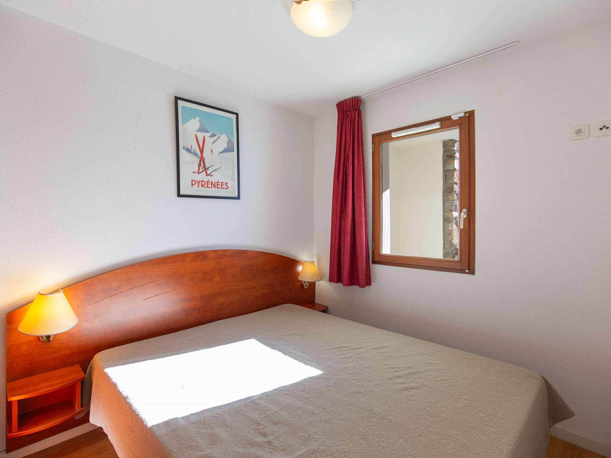 Une chambre à coucher avec un lit, une table de chevet, une lampe, une fenêtre avec un rideau et une affiche accrochée au mur.