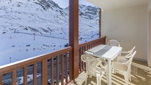 A balcony with a table and chairs, overlooking a snowy mountain landscape. - Pleasant T2, parking - 4 guests (La Mongie)