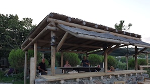Ett rustikt utomhusområde med bar, en vägg av sten, träbänkar och en pergola av trä.