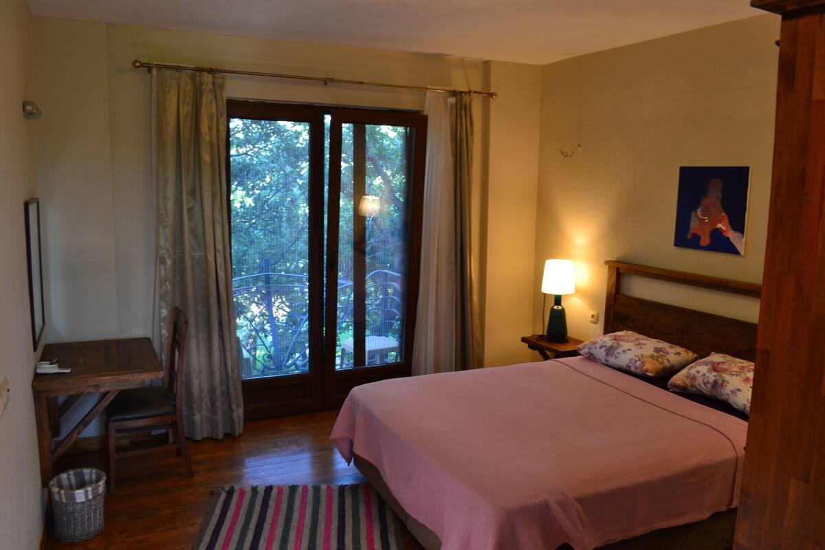 A bedroom with a bed, a desk, a chair, a lamp, and a window with curtains.