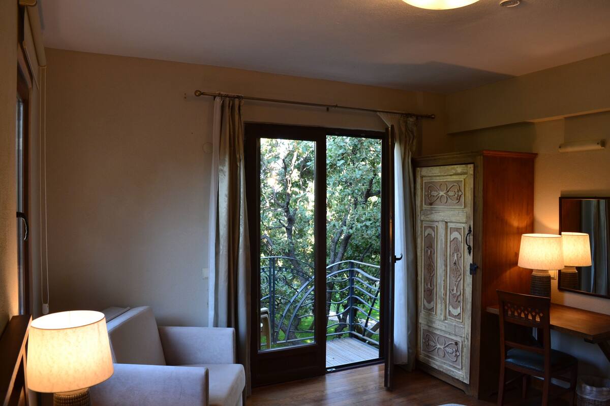 A room with a sofa, a table with lamps, a wooden desk, and a door leading to a balcony with a metal railing.