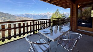 Un balcón de madera con una mesa y sillas, con vistas a un paisaje montañoso.