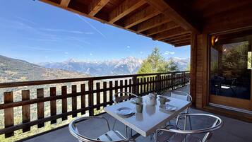 Ein Holzbalkon mit Tisch und Stühlen, mit Blick auf eine Berglandschaft.